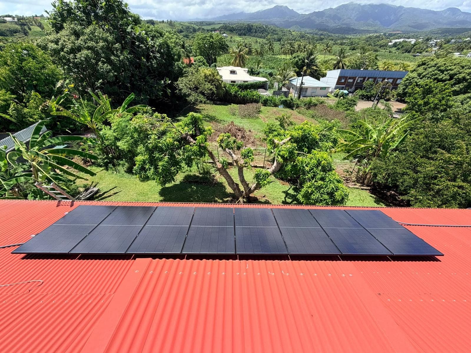 Panneaux solaires photovoltaïques posés par FRH sur une toiture en tôle rouge en Guadeloupe, vallée et mornes en arrière-plan